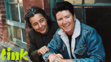 Die zwei Hauptpersonen des Film hocken lächelnd vor einem Fenster und schauen in die selbe Richtung