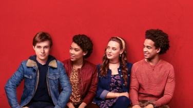 Film still: Simon is sitting on a bench with three friends.